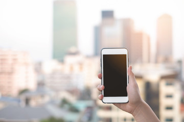 hand holding smartphone or mobile phone with city building background and copy space.