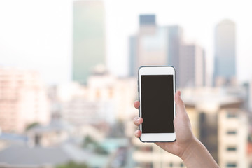 hand holding smartphone or mobile phone with city building background and copy space.