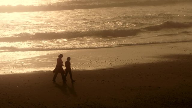 Two women walking on empty beach at sunrise or sunset. Silhouetted.