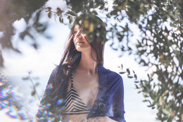 Beautiful brunette girl, portrait through the trees on a background of nature. Spring, beauty, fashion concept