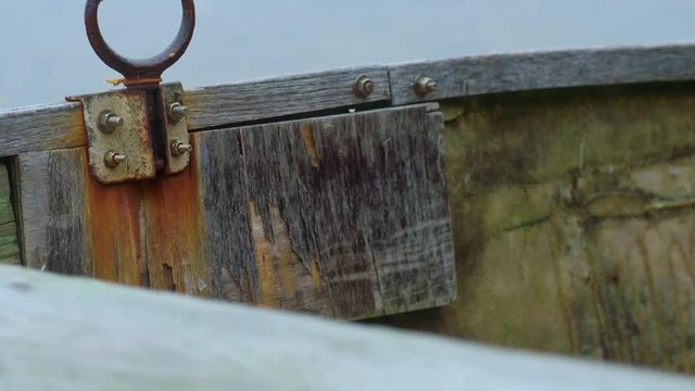 Tight closeup of rusty old oarlock on a wooden rowboat. Cobwebs. Camera tilts up.