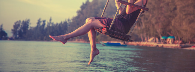 slender female legs close up, woman swinging on a swing on the beach during sunset, rest, travel, lifestyle concept - obrazy, fototapety, plakaty