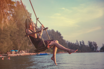 Young beautiful happy woman swinging on a swing on the beach during sunset, relaxing travel...