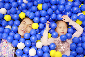 Fototapeta na wymiar Portrait of mother and little girl playing with color plastic balls playground.