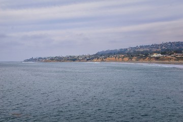 View from Mission Beach in San Diego, of Piers, Jetty and sand, around surfers, including warning signs, palm trees, waves, rocks, boats and horizon views. Pacific Ocean. California, United States.