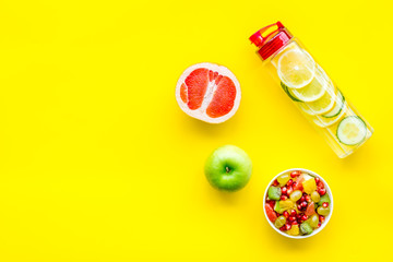 Diet rich in fruits. Slimming diet. Fruit salad near fruit lemon and cucumber water on yellow background top view copy space