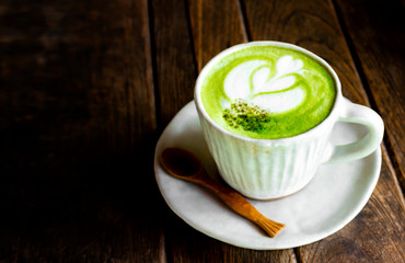 Hot matcha green tea latte with milk foam in a white cup on old wooden table, A cup of green tea latte coffee art, top view on wooden plate