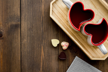 Valentine's day concept. Heart-shaped mugs and sweets on dark wooden background top view space for text