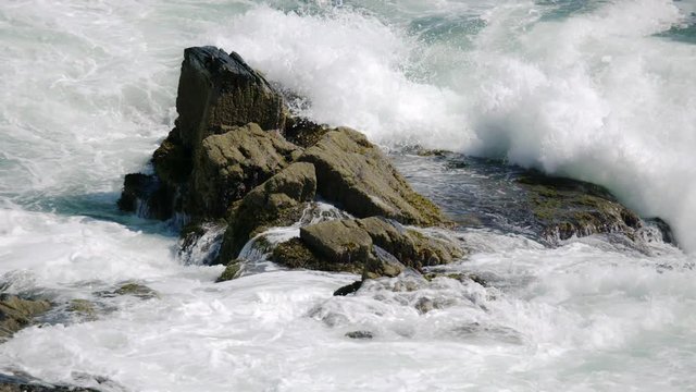 Ocean waves crashing onto rocky shoreline and water spray going in all direction in 180 fps slow motion
