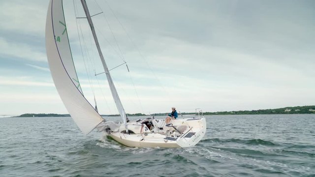 Professional solo sailor sailing on the ocean in a racing sailboat. Adjusting the ropes and steering with the rudder.  Shot from behind from a chase boat.