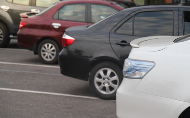 Closeup of rear side of white car and other cars parking in parking lot in the evening of sunny day. 