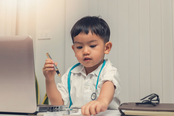 Young asian boy playing doctor and using computer laptop.