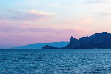 Beautiful view of the evening sunset in Sudak, Crimea. Sunset on the sea horizon with mountains and red clouds.