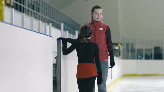 Tilt down shot of professional figure skater meeting her trainee on ice inside arena and starting exercise