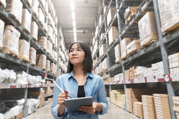 Candid of young attractive asian woman auditor or trainee staff work looking up stocktaking inventory in warehouse store by computer tablet with wide angle view. Asian owner or small business concept.