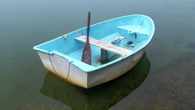 Dinghy rowboat at anchor in a quiet foggy cove.