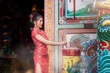 Concept to celebrate Chinese New Year : Chinese woman in a red cheongsam dress holding incense pay homage to Chinese god at shrine.