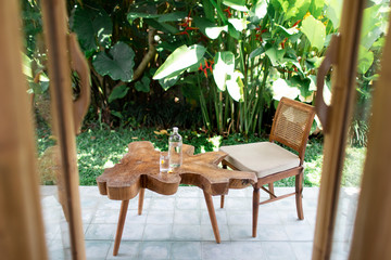 Table from tree stump with glass bottle of water standing it home terrace. Unmanufactured and cracked wood massif of the table. Artistic processing of wood. Loft furniture. Modern furnishings.