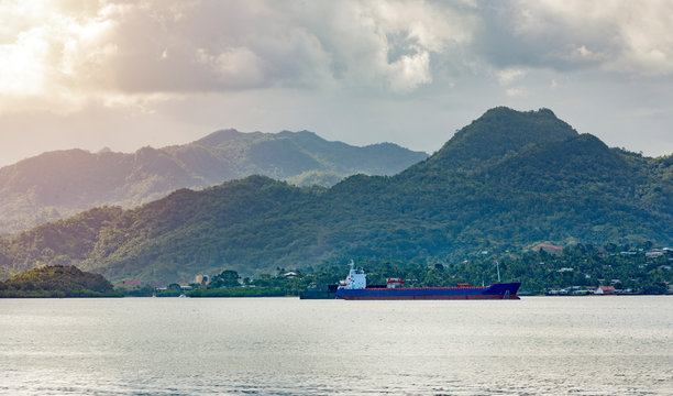 Empty Cargo ship running though in bay at Fiji country. mountains and small community are background with moody clouds during sunset.