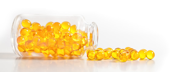 Yellow pill capsules crumble from a glass bottle on a white background.