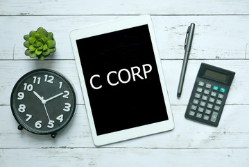 Business concept. Top view of plant,clock,calculator,pen and tablet written with C Corp on white wooden background,