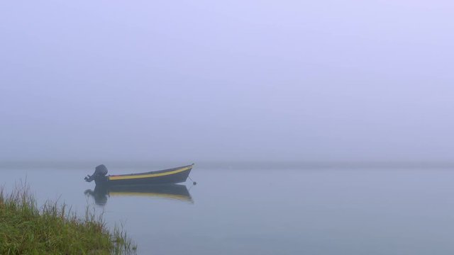 Black and yellow dinghy fishing boat at anchor in a quiet foggy cove with calm water and dune grass.