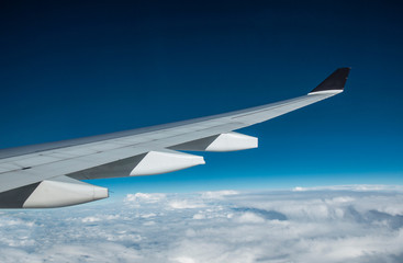 white and black color airplane wing from window and flying above white clouds with blue sky. Blue theme.