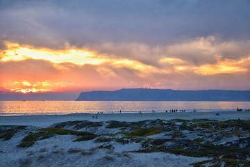 Obraz premium Coronado Beach in San Diego by the Historic Hotel del Coronado, at sunset with unique beach sand dunes, panorama view of the Pacific Ocean, silhouettes of people walking and boats in California, Unite