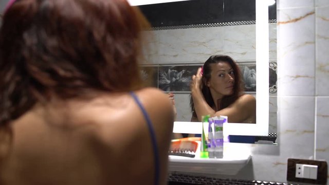 Woman combing hair in front of a mirror in the bathroom