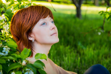 Girl with red hair in the park with blooming apple trees. Portrait of ordinary girl. Harmony concept