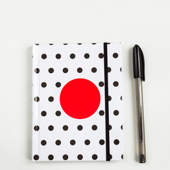 Black and white polka dot note book with red circle  on the cover and black pen on white table. top view, minimal flat lay