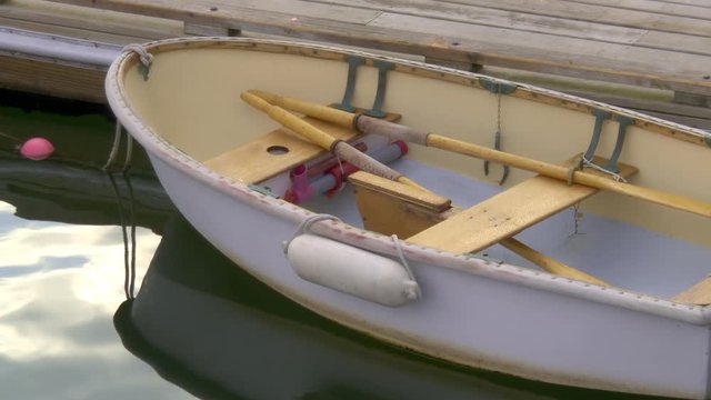 Classic wooden fishing boat dinghy tied up to a dock in New England fishing village harbor.  Wooden paddles and oars,