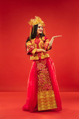 Chinese traditional graceful woman at studio over red background. Beautiful girl wearing national costume. Chinese New Year, elegance, grace, performer, performance, dance, actress, dress concept