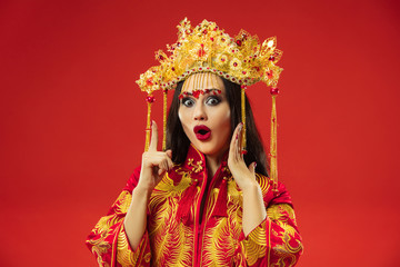Chinese traditional graceful woman at studio over red background. Beautiful girl wearing national costume. Chinese New Year, elegance, grace, performer, performance, dance, actress, emotions concept