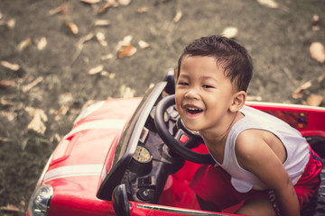 Little boy driving car with the steering wheel. Boy in a white shirt in a red toy car in the street. Little boy driving big toy car and having fun, outdoors.