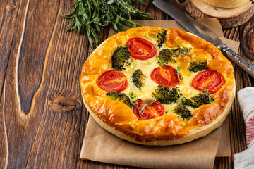 Vegetable pie with broccoli, peas, thyme. tomatoes and cheese on wooden background. Copy space.