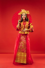 Chinese traditional graceful woman at studio over red background. Beautiful girl wearing national costume. Chinese New Year, elegance, grace, performer, performance, dance, actress, emotions concept