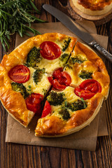 Vegetable pie with broccoli, peas, thyme. tomatoes and cheese on wooden background. Copy space.