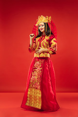 Chinese traditional graceful woman at studio over red background. Beautiful girl wearing national costume. Chinese New Year, elegance, grace, performer, performance, dance, actress, emotions concept