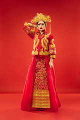 Chinese traditional graceful woman at studio over red background. Beautiful girl wearing national costume. Chinese New Year, elegance, grace, performer, performance, dance, actress, emotions concept