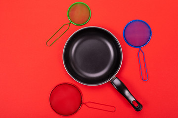 Frying pan in the center with cooking utensils around isolated on red background