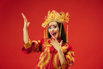 Chinese traditional graceful woman at studio over red background. Beautiful girl wearing national costume. Chinese New Year, elegance, grace, performer, performance, dance, actress, emotions concept