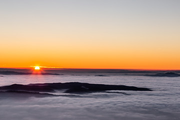 Obraz premium Beautiful sunset over a valley filled by fog with mountains and hills