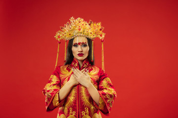 Chinese traditional graceful woman at studio over red background. Beautiful girl wearing national costume. Chinese New Year, elegance, grace, performer, performance, dance, actress, dress concept