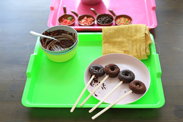 Homemade chocolate donuts in process on wooden table.