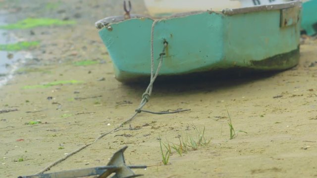 Peaceful shot of rustic wooden rowboat dinghy beached on sandy shore on Cape Cod. Camera tilts up from the anchor embedded in the sand to reveal the boat.
