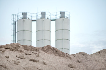 Large piles of construction sand and gravel used for asphalt production and building. Limestone quarry, mining rocks and stones. Factory in the background. Empty space for text of logo  