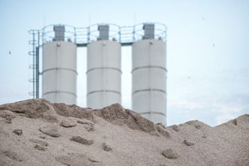 Large piles of construction sand and gravel used for asphalt production and building. Limestone quarry, mining rocks and stones. Factory in the background. Empty space for text of logo  