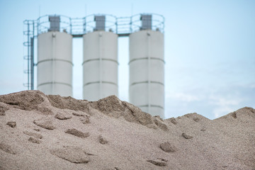 Large piles of construction sand and gravel used for asphalt production and building. Limestone quarry, mining rocks and stones. Factory in the background. Empty space for text of logo  