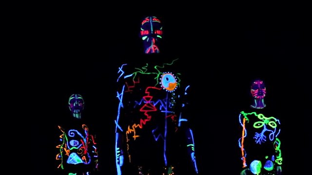group of children performs performances in a dark hall, in colorful costumes. Paint in costumes shines in the dark. Choreographic setting of a group of children